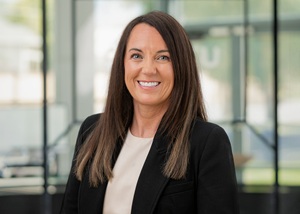 UTOPIA Fiber Dep Director Nicole Cottle smiles in lobby of UTOPIA Fiber building, wearing a black blazer and long brunette hair
