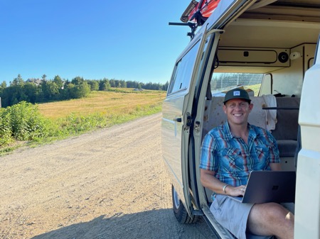 MCA President Andrew Butcher seated in back of yellow Volkswagen van with a laptop on his lap smiling at camera
