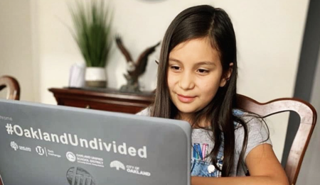 Little girl sits at desk behind a laptop provided by #OaklandUndivided