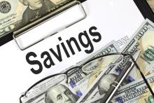 Image of clipboard with the word "savings" at top, surrounded by hundred dollar bills and a pair of glasses