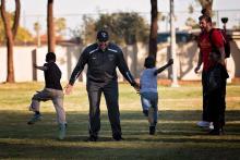 Two young kids with their backs to the camera reach the finish line in a community race greeted by two happy adults celebrating their run