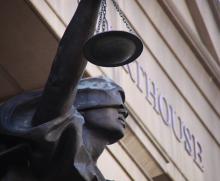 Statue of blindfolded woman holding scales of Justice in front of courthouse